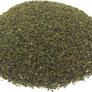 May include: A pile of dried, green, chopped herbs, possibly for culinary use. The herbs are a deep green color and appear to be finely cut, creating a textured surface. The image is a close-up, showing the details of the dried leaves.
