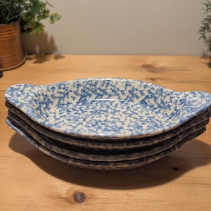May include: A stack of five oval serving dishes. Each dish features a blue and white speckled pattern and handles at each end. The dishes are stacked on a wooden surface.