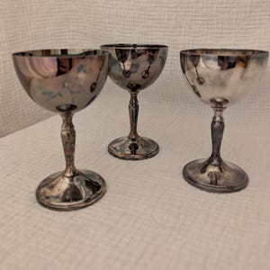 Puede incluir: Tres copas de plata con un diseño clásico. Las copas están hechas de metal pulido y tienen una copa redonda y un tallo alto.