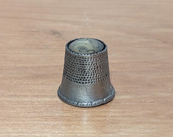 May include: A silver thimble with a textured surface and a decorative design on the top.