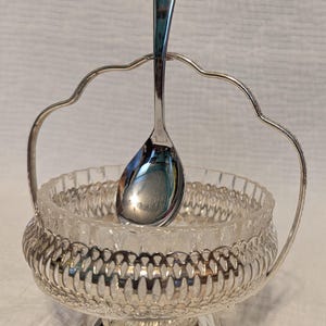 May include: Silver sugar bowl with a glass insert and a matching spoon. The bowl has a decorative, openwork design.