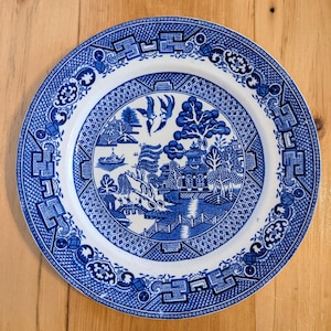 以下が含まれることがあります： 柳の模様が描かれた青と白のセラミック製のディナー皿。皿には、様式化された柳の木、パゴダ、橋が描かれています。
