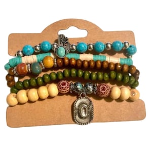 May include: A set of five beaded bracelets in various colors, including turquoise, brown, green, and cream. The bracelets feature a mix of wooden and metal beads, with a silver-tone charm of a cowboy hat. The bracelets are displayed on a brown cardboard backing.