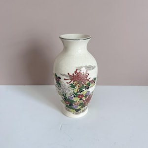 Può includere: Vaso in ceramica color crema con bordo argentato e motivo floreale. Il vaso presenta un motivo dettagliato di fiori rossi, bianchi, verdi e viola. Il vaso ha una superficie leggermente strutturata e una forma classica, per l'arredamento.