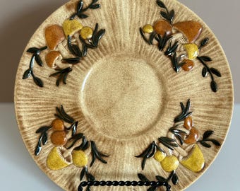May include: Tan ceramic plate with a raised mushroom and leaf design. The plate features brown, yellow, and green accents. The plate is round with a central recessed area and a textured surface.
