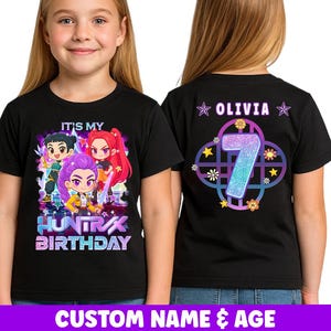 Puede incluir: Camiseta negra con un gráfico colorido con personajes de estilo anime y el texto "IT'S MY HUNTRAX BIRTHDAY" en la parte delantera. La parte trasera de la camiseta muestra el nombre "OLIVIA" y el número "7" con detalles florales y de estrellas.