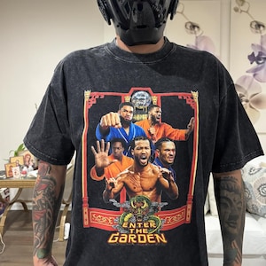 以下が含まれることがあります： 黒いアシッドウォッシュ加工のTシャツで、武道のポーズをとった5人のバスケットボール選手のグラフィックプリントが施されています。デザインには赤いフレーム、ドラゴンのイラスト、そして下部に黄色の文字で「ENTER THE GARDEN」と記されています。