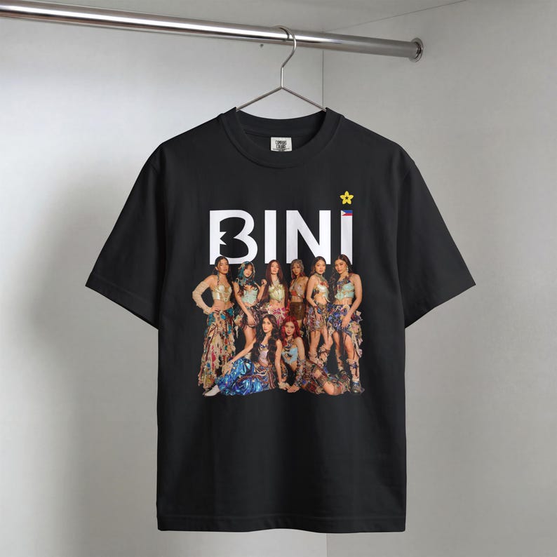May include: A black short-sleeved t-shirt featuring a large white graphic print of the word BINI with a yellow star and a small Philippine flag. Below the text is a full-color photographic image of a group of eight individuals in outfits.