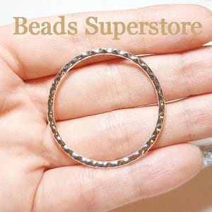 May include: A circular metal ring connector with a textured, hammered surface finish. The piece features a metallic silver tone and is presented with the text Beads Superstore visible in the background. The design is simple and round.