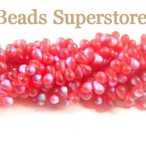 May include: A collection of small, teardrop-shaped beads in a vibrant red hue with a frosted, iridescent finish. The beads are arranged in a dense, horizontal cluster. The text "Beads Superstore" is printed in a light brown font above the beads.