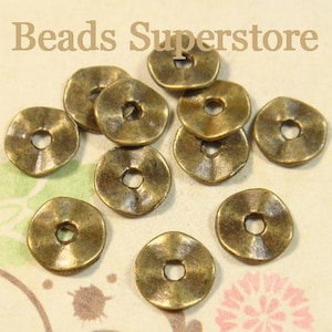 May include: A collection of small, round, antique brass-colored metal spacer beads with a wavy, hammered texture and a central hole. The text "Beads Superstore" is visible at the top of the image. These circular metal components have a distressed finish.