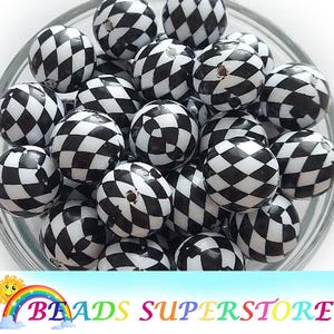 May include: A collection of spherical beads featuring a black and white diamond checkerboard pattern. Each bead has a small hole visible at the top, and they are grouped together in a clear container. The surface of the beads is smooth and glossy.
