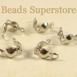 May include: Five silver-toned metal bead tips or clamshell knot covers arranged in a cluster. Each piece features a rounded center with a small loop at each end for jewelry making. The text Beads Superstore is visible at the top of the image.