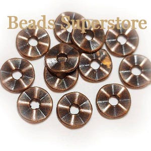 May include: A collection of round, copper-colored metal beads with a central hole and a textured, radial grooved pattern on the surface. The text "Beads Superstore" is printed in light brown across the top of the image over the metal beads.