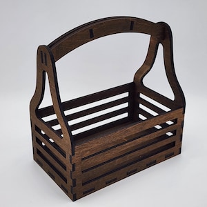 Può includere: Un cesto in legno marrone scuro con manico. Il cesto ha una forma rettangolare con doghe orizzontali e un manico curvo. Il design è semplice e funzionale.
