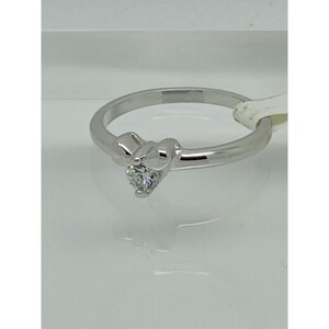May include: A silver ring with a small, clear gemstone. The ring has a unique design with a decorative element near the gemstone. The ring is displayed on a white surface.