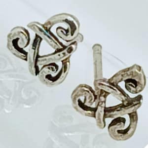 May include: A pair of silver-colored stud earrings. Each earring features an intricate, swirling design with a textured finish. The earrings are displayed against a white background, highlighting their detailed craftsmanship.