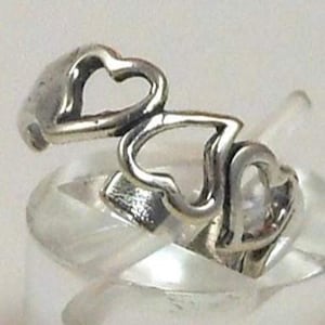 May include: A silver ring featuring three open heart designs. The ring is made of a shiny, metallic material and has a simple, elegant style. The hearts are connected, creating a unique and romantic look. The ring is likely a fashion accessory.