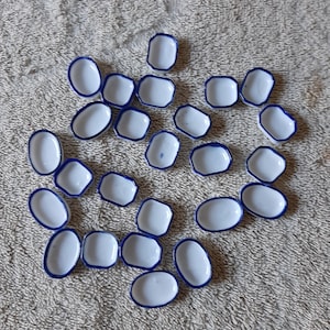 May include: A collection of small, white ceramic dishes with a blue trim. The dishes are oval and rectangular, and are arranged on a textured, light-colored surface. The dishes are empty.