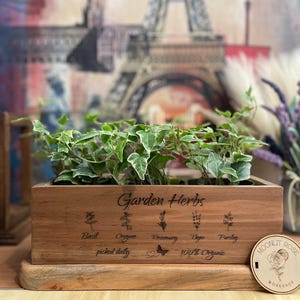 May include: A wooden box with a variety of herbs growing inside. The box is labeled "Garden Herbs" and lists the herbs as Basil, Oregano, Rosemary, Thyme, and Parsley. The box also says "picked daily" and "100% Organic".