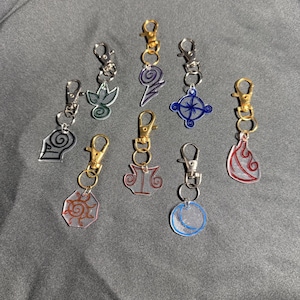 May include: A collection of keychains with various designs, including a sun, moon, and other abstract shapes. The keychains have gold and silver-colored clasps and are made of clear acrylic with colorful accents.