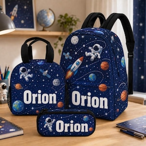 May include: A dark blue backpack, lunch bag, and pencil case set featuring a space-themed pattern with astronauts, rockets, planets, and stars. Each item displays the name Orion in bold white letters across the front in a clear, sans-serif font.