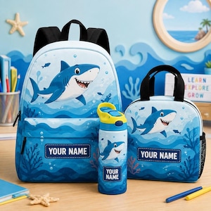May include: A light blue backpack, a matching lunch bag, and a water bottle, all featuring a cartoon shark print, underwater coral motifs, and a rectangular label with the text YOUR NAME on each item. The items have black straps and accents.