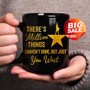 May include: Black ceramic mug with gold text that reads "THERE'S Million THINGS I HAVEN'T DONE, BUT JUST You Wait." A gold star and silhouette are also featured. A red and orange "BIG SALE" sticker is on the right side.