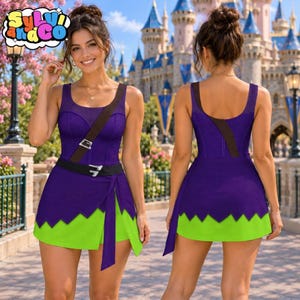 May include: A purple and lime green sleeveless dress featuring a scoop neckline, a dark brown diagonal strap with a silver buckle, and a jagged hemline. The dress has a fitted bodice and a wrap-style skirt with a tie detail on the front side.