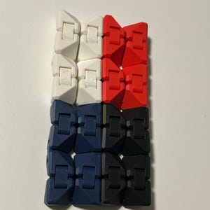 Puede incluir: Un colorido juguete fidget compuesto por bloques entrelazados en blanco, rojo, azul marino y negro. Los bloques están dispuestos en forma rectangular, ofreciendo una experiencia táctil y atractiva. El diseño del juguete es visualmente atractivo y adecuado para aliviar el estrés.