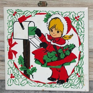 May include: A vintage Christmas tile depicting a girl in a red coat and hat posting a letter in a white mailbox. The design includes holly and a red ribbon border, with a metal hanger at the top. The tile is square.