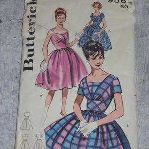 May include: Vintage Butterick sewing pattern featuring illustrations of women's dresses. The pattern cover displays drawings of dresses in pink, blue, and plaid designs. The text includes "BUST 32 SIZE 12" and the pattern number "956".