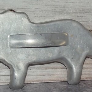 Puede incluir: Un cortador de galletas vintage con forma de león de color plateado. El cortador de metal tiene un asa rectangular y está diseñado con una melena, un cuerpo y patas detallados. El cortador de galletas probablemente se utiliza para hornear.