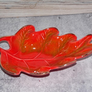 May include: A ceramic leaf-shaped dish in a vibrant red hue with gold trim. The dish features a handle and detailed leaf vein patterns. This decorative piece is suitable for serving or display.