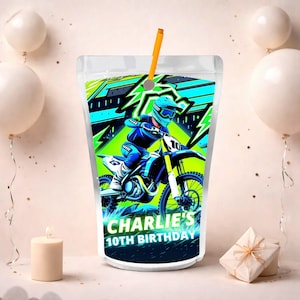 Pode incluir: Uma embalagem de suco transparente com canudo, apresentando um piloto de motocross em uma moto azul e amarela. O design inclui detalhes em verde e azul, com o texto "Charlie's 10th Birthday" na parte inferior.