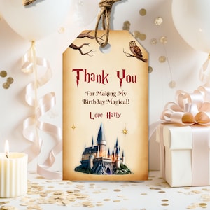 Puede incluir: Una etiqueta de regalo de estilo vintage con el texto "Thank You For Making My Birthday Magical! Love Harry" en una fuente gótica. La etiqueta presenta una ilustración de un castillo, un búho y una rama. Está atada con un cordel natural.