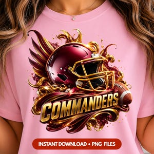 May include: A light pink t-shirt featuring a graphic of a burgundy football helmet with a gold face mask, surrounded by swirling gold and burgundy accents, a football, and the word COMMANDERS in bold gold lettering with a drop shadow effect.