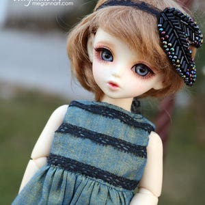 May include: A doll wearing a blue and black striped dress with black lace trim. The doll has brown hair, blue eyes, and is wearing a black headband with a black feather accent. The text "PDF Digital Pattern" is at the bottom of the image.