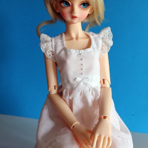 May include: A white dress with lace trim and a bow at the waist. The dress is worn by a doll with blonde hair and blue eyes. The doll is sitting on a blue background. The text "PDF Digital Pattern" is at the top of the image. The text "MegannArt megannart.com" is at the bottom of the image.