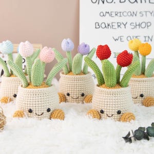 Könnte beinhalten: Gehäkelte Tulpen-Blumentöpfe in verschiedenen Farben, darunter Rot, Gelb, Rosa, Blau und Lila. Jeder Topf hat ein lächelndes Gesicht und hellbraune Füße. Im Hintergrund steht ein Schild mit der Aufschrift "UNO. BAKERY AMERICAN STYLE BAKERY SHOP PARIS WE ARE IN PARIS."