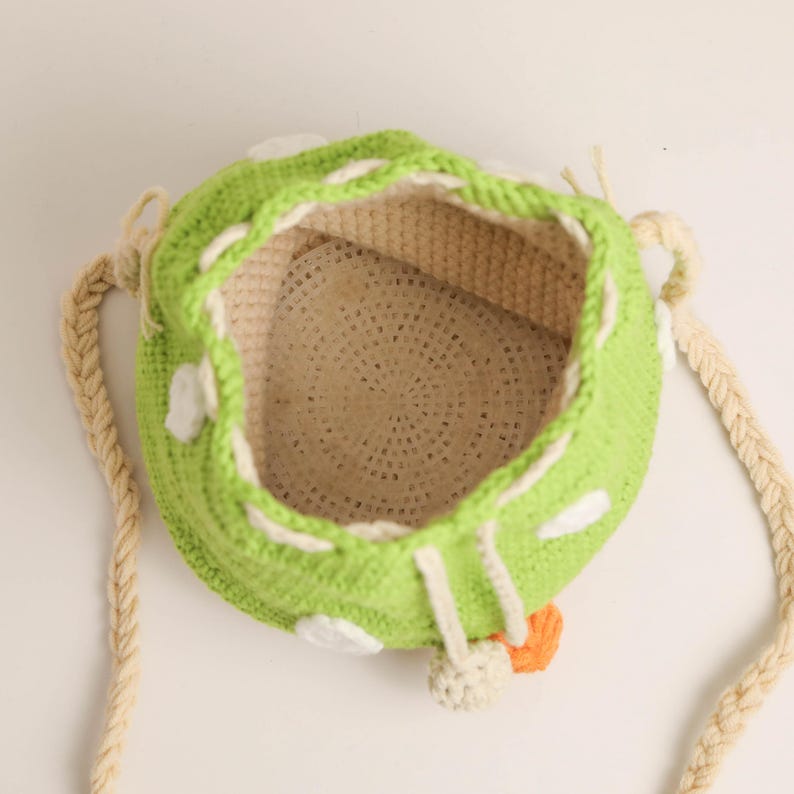 May include: A handmade green crochet bag with white polka dots and a beige interior. The bag has a drawstring closure and a braided beige strap. An orange accent is visible near the bottom.