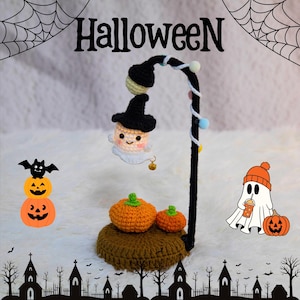 May include: A crochet Halloween-themed display featuring a black lamp post with a smiling ghost wearing a witch hat. Two orange pumpkins sit on a brown base. The word "Halloween" is at the top.