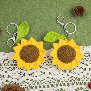 May include: Two handmade crochet sunflower keychains. Each keychain features a yellow sunflower with a brown center and a green leaf. The keychains have silver-colored metal hardware.