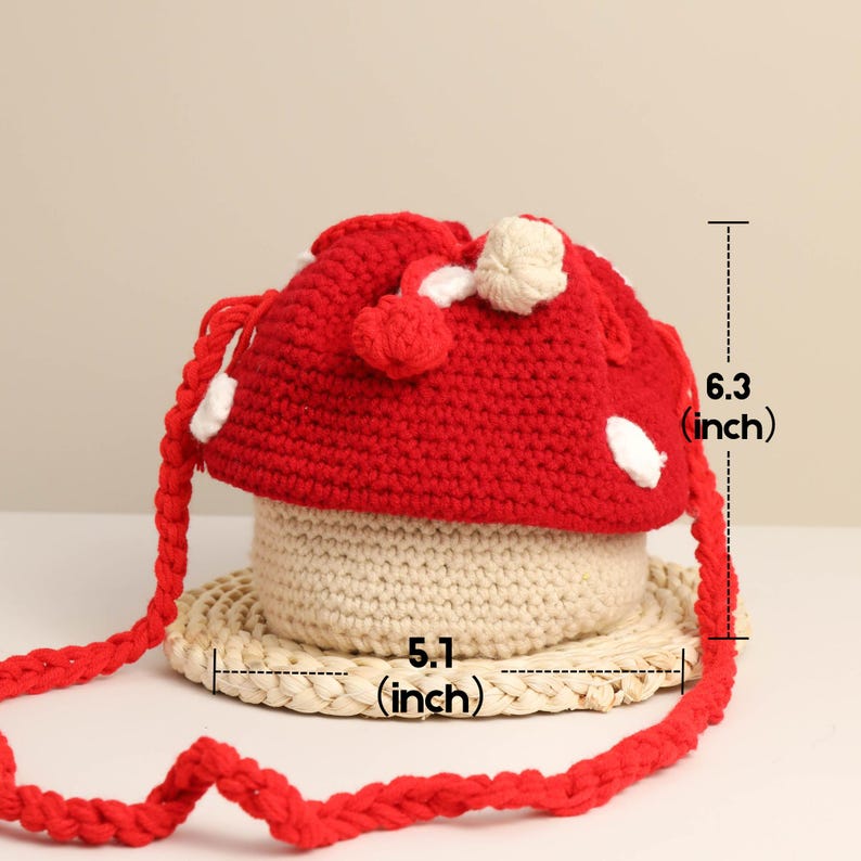 May include: A red and white mushroom-shaped crochet bag with a beige base and a woven straw-like base. The bag is 6.3 inches tall and 5.1 inches wide. The bag has a red braided strap.
