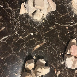 May include: Two piles of broken white and light brown clay on a black marble surface.
