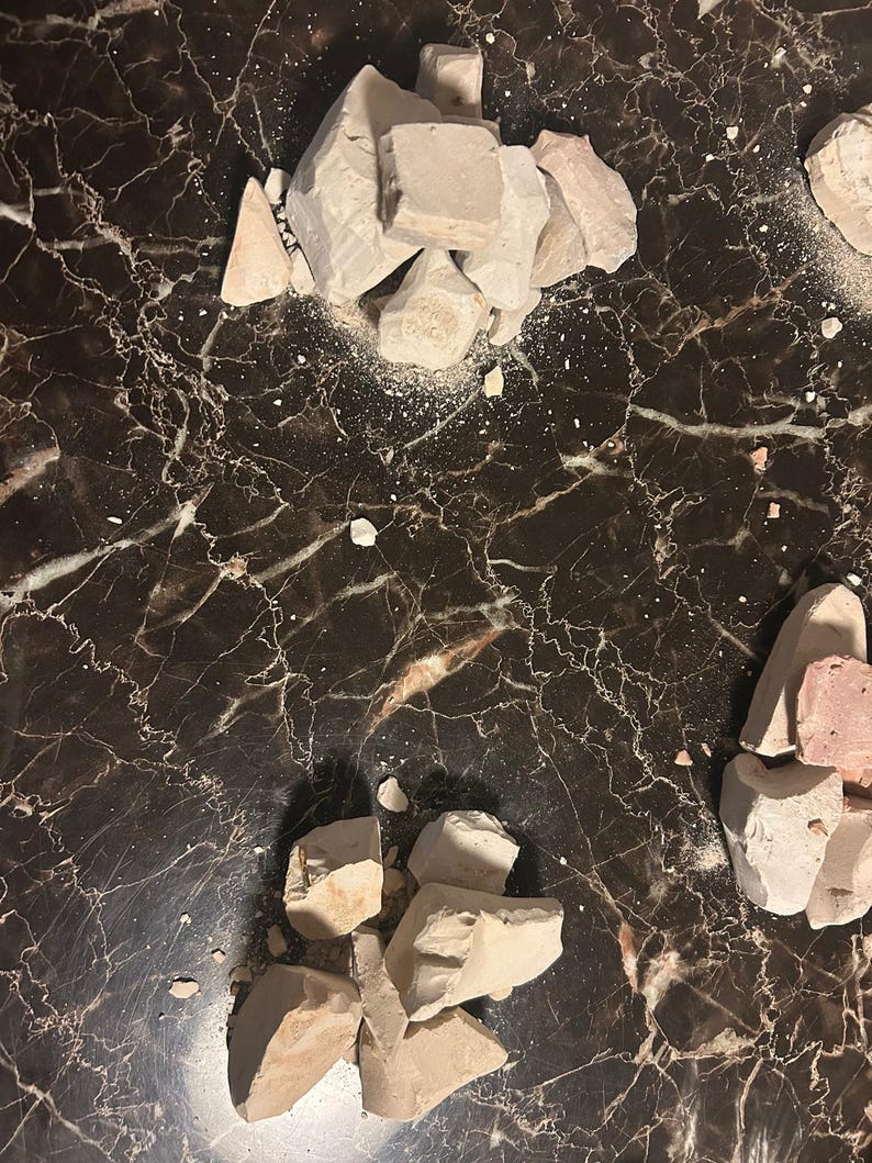 May include: Two piles of broken white and light brown clay on a black marble surface.