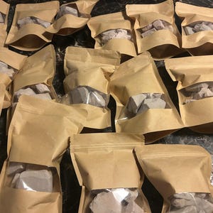 May include: Multiple brown paper bags with clear plastic windows, each containing a variety of small, irregularly shaped, light gray rocks.