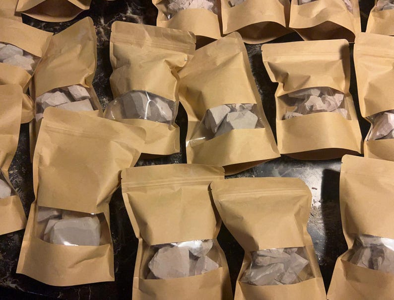 May include: Multiple brown paper bags filled with white clay chunks. The bags are sealed and have a clear window to see the contents.