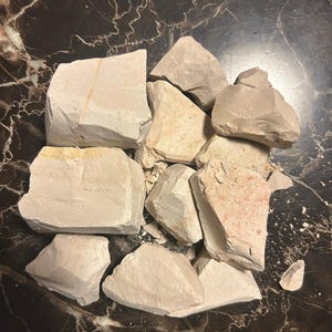 May include: A pile of broken, light brown clay chunks on a dark brown marble surface.