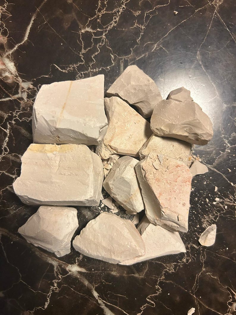 May include: A pile of broken, light brown clay chunks on a dark brown marble surface.